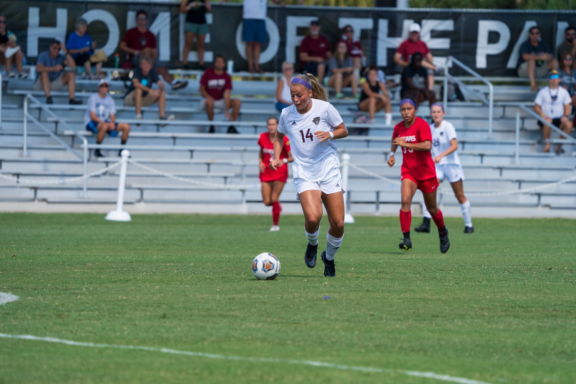 Florida Tech women's soccer player dribbling the ball during a match, with spectators in the background watching the game